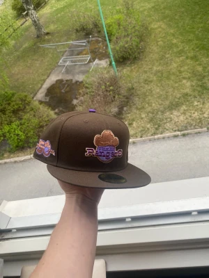 Helt ny New era Texas Rangers keps - Texas Rangers keps från New Era med broderad logga framtill och 50-årsjubileumsmärke på sidan. Flat peak och klassisk 59FIFTY-modell. Kepsen har lila och guld detaljer och är tillverkad i ett slitstarkt tyg. Den är helt ny aldrig använd och säljs på grund av att den var för stor! Storlek 7 1/2 vilket motsvarar 59,6cm. Hör av er vid frågor! 