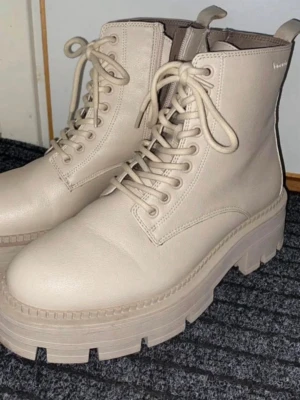 Vinterskor - Tamaris - Säljer ett par beige chunky kängor från DinSko med grov sula och snörning framtill. Insidan är fodrad med mjukt beige fuskpälsfoder för extra värme. Perfekta för kalla dagar och ger en trendig look till din outfit.