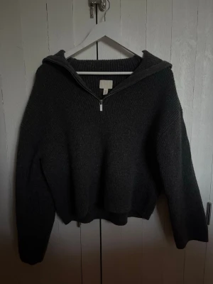 Mörkgrå stickad tröja med dragkedja - Mysig mörkgrå stickad tröja från H&M med halv dragkedja framtill och krage. Tröjan har en avslappnad passform och långa ärmar, perfekt för lager-på-lager-stil. Materialet är mjukt och ger en skön känsla hela dagen.