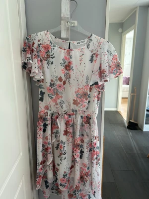 Blommig sommarklänning från H&M 🩷 - Söt blommig klänning från H&M i vitt med rosa och blå blommor. Klänningen har volangärmar, rund halsringning och knytband i midjan. Lätt och luftig modell, perfekt för varma dagar.