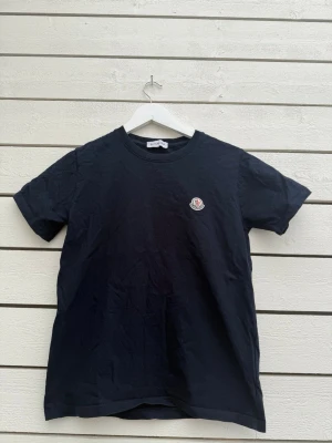 Svart Moncler t-shirt med logga - Snygg svart t-shirt från Moncler med klassisk rund hals och korta ärmar. På bröstet sitter Monclers ikoniska logga i vitt, rött och blått. Perfekt basplagg med exklusiv känsla och stilren design.