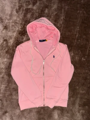 Rosa hoodie från Polo Ralph Lauren XS - Snygg rosa hoodie från Polo Ralph Lauren med dragkedja och huva. Klassisk logga broderad på bröstet och vita snören i huvan. Perfekt för en avslappnad och trendig stil. Storlek och mått kan informeras privat. Pris kan Diskuteras. 😊