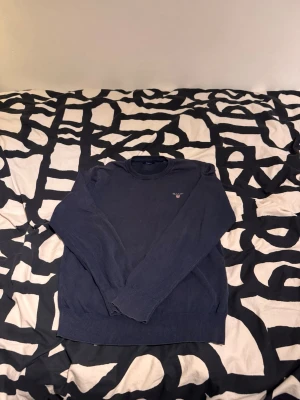 Mörkblå tröja från Gant - Mörkblå långärmad tröja från Gant med rund halsringning och diskret logga broderad på bröstet. Tröjan har ribbade muddar vid ärmslut och nederkant. Har även sytt tröjan då den gick sönder men det är inget som man ser när den är på. En tröja som är perfekt för en stilren och enkel look. 