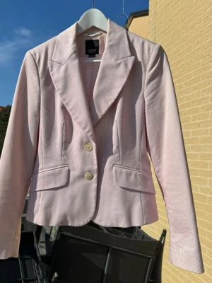 Ljusrosa kavaj från Esprit - Snygg ljusrosa kavaj från Esprit med diskreta vita ränder. Klassisk modell med två knappar framtill, spetsiga slag och fickor med lock. Perfekt för en stilren look & snygg till jeans.