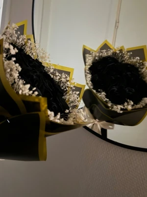 Bukett med svarta rosor och vita detaljer - Snygg bukett med svarta konstgjorda rosor, omgiven av små vita torkade blommor. Buketten är inslagen i svart och gult papper och knuten med ett vitt band. Perfekt som unik dekoration eller present.