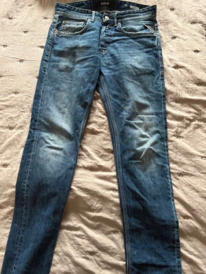 Blå raka jeans från Replay - Snygga blå jeans från Replay med raka ben och klassisk femficksmodell. Jeansen har slitningar och ljusare partier framtill för en cool, avslappnad look. Tillverkade i denim med detaljerade sömmar och metallknappar.