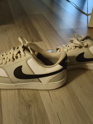 Vita NIKE COURT VISION LO Sneaker Strlk 43 - Snygga vita sneakers från Nike med klassisk svart swoosh på sidan. Skorna har lågt skaft, vita snören och perforerad tå för extra ventilation. Ovandelen är i läder och textil, vilket ger både stil och komfort. Perfekta för dig som gillar en clean och sportig look. Skorna är i fint skick, storlek 43. Nypris runt 900:-