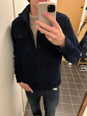 Mörkblå overshirt från Jack & Jones - Säljer en mörkblå overshirt från Jack & Jones i manchestertyg. Skjortjackan har knappstängning, bröstficka med lock och klassisk krage. Perfekt att bära över en tröja för en avslappnad och snygg look.