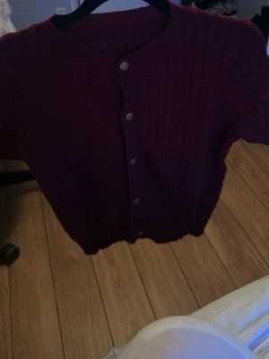 Mörklila kortärmad kofta - Kortärmad kofta i mörklila med rund halsringning och knappar framtill. Stickad struktur och ribbade kanter ger en snygg och enkel look. Perfekt att slänga över en topp för en chill stil.