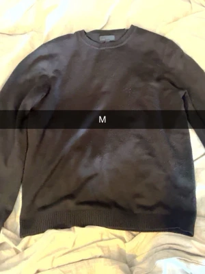 Svart stickad basic rundhalsad tröja M från ASOS - En stilren stickad svart tröja med rund halsringning och långa ärmar. Tröjan har ribbade muddar vid ärmslut och nederkant, perfekt för en enkel och clean look. Passar till det mesta och är lätt att matcha med andra plagg.