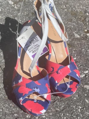 kilklack-sandaler Tommy Hilfiger - Säljer ett par kilklack-sandaler från Tommy Hilfiger med coolt mönster i rött, blått och vitt. Skorna har vita remmar och öppen tå, perfekt för dig som vill sticka ut. 