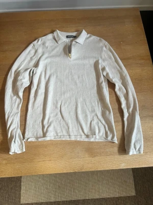 Beige långärmad tröja med dragkedja - Stilren beige långärmad tröja med krage och kort dragkedja framtill. Perfekt för lager-på-lager och enkel att matcha med olika outfits. Mjuk och lätt materialkänsla, passar både till jeans och chinos.
