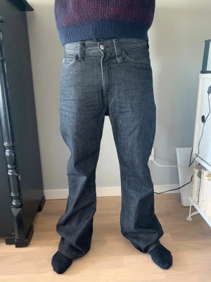 Mörkgråa jeans  - Säljer ett par mörkgråa jeans med hög midja. Jeansen har klassisk femficksdesign, knappgylf och långa ben som ger en avslappnad look. Perfekta för dig som gillar en tidlös och enkel stil.