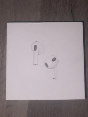 Apple AirPods 3 trådlösa hörlurar - Säljer ett par vita Apple AirPods 3 med laddningsetui. De är trådlösa in-ear-hörlurar med stilren design och smidigt fodral. Perfekta för musik, samtal och träning. Klassisk Apple-kvalitet och snygg form som passar i fickan.