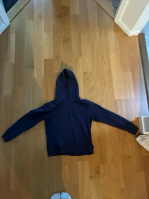 Mörkblå hoodie från GANT - Säljer en mörkblå hoodie från GANT med broderad logga och texten 'American Sportswear' på bröstet. Klassisk huva och långa ärmar, perfekt för en avslappnad och sportig stil. Skön och mjuk bomullsblandning. Väldigt fin tröja! 