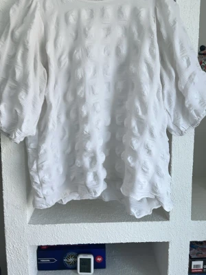 Vit strukturerad blus från Isolde - Vit blus från Isolde med unik struktur och mönstrad yta. Blusen har trekvartsärm och en lös, bekväm passform. Perfekt för dig som gillar stilrena och moderna plagg med det lilla extra. Tillverkad i ett mjukt och lätt material.