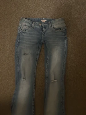 Ljustblåa Gina tricot bootcut  - Säljer ett par ljusblå bootcut jeans med slitningar på benen och broderad bakficka. Jeansen har klassisk femficksdesign och snygg tvättad look. Perfekta för en avslappnad och trendig stil. Ordinarie pris 429kr säljer för 300kr (pris kan diskuteras)💕