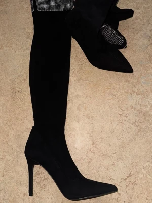 Svarta overknee stövlar med klack - Snygga svarta overknee stövlar med spetsig tå och hög smal klack. Stövlarna är i mockaimitation och har en tight passform längs benet. Perfekta för att lyfta din outfit med en trendig och elegant look.