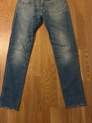 Ljusblå  jeans från Replay - Säljer ett par ljusblå jeans från Replay med raka ben och klassisk femficksdesign. Jeansen har slitna detaljer vid fickorna och en snygg tvättad look. Perfekta för en avslappnad stil och passar till det mesta.