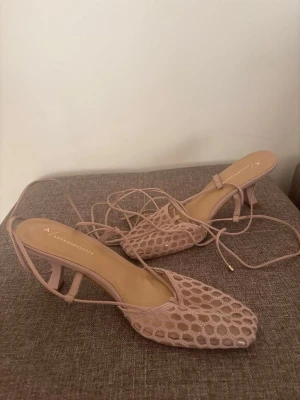 Anthropologie klackakor - Klackskor med snörning som knyts runt ankeln. Skorna har en öppen design med ett nätmönster över foten och en stabil klack. Skorna är små i storleken 