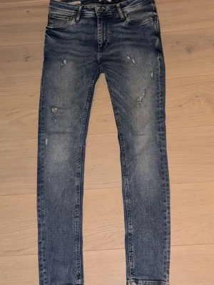 Slim fit blå slitna jeans - Snygga slim fit jeans i blå denim med slitningar och lätt tvättad look. Klassisk femficksmodell med dragkedja och knapp. Perfekta för en avslappnad och trendig stil.