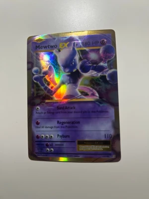 Pokémonkort Mewtwo EX holografisk - Säljer ett Pokémonkort med Mewtwo EX, holografisk yta som skimrar i regnbågens färger. Kortet har 180 HP och attacker som Sand Attack, Regeneration och Psyburn. Perfekt för samlare eller Pokémonfans.