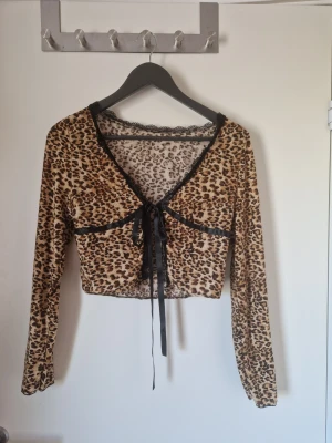 Leopard mönstrad blus - Leopard mönstrad blus med svart spets detaljer och svarta band i satin liknande material som man själv kan knyta. Storlek M. Lite liten vid bysten för mig som är en C kupa. I ett tunt och mjukt material. I fint skick köpt på sellpy. Katt finns i hemmet. 