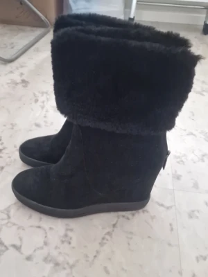 Svarta fluffiga kilklackstövlar - Säljer ett par svarta stövlar med kilklack och bred, fluffig fuskpälskant upptill. Stövlarna har en mjuk yta och dragkedja på sidan. Perfekta för kalla dagar när du vill vara både varm och snygg. Storlek 39. Pris kan diskuteras🫶🏼❤️