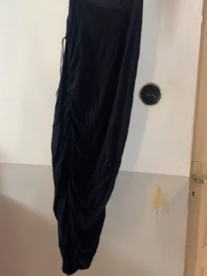 Svart långklänning från Pieces - Säljer en svart långklänning från Pieces. Klänningen har en åtsittande passform och är tillverkad i ett mjukt, stretchigt material. Perfekt för dig som gillar en stilren och enkel look. Klänningen har snygga draperingar längs sidorna.