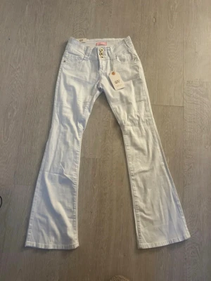 Vita bootcut jeans från girl vivi (sprillans nya) - Snygga vita bootcut jeans från GV med tre guldfärgade knappar framtill och klassiska fickor. Jeansen har en utsvängd passform och är tillverkade i ett mjukt denim-material som känns bekvämt. Perfekta för dig som vill ha en cool och trendig look. Midjemåttet är ca 35cm rakt över men de är även stretchiga. 
