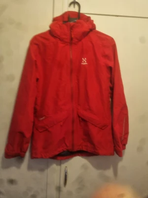 Haglöfs Skaljacka Junior stl 164 - Snudd på oanvänd Haglöfs Skaljacka med luva. . 100% vatten och vindtät.  Stängs med dragkedja och kardborre knäppning framtill. 2 fickor fram Dragsko för reglering av jackans nedre del.                      Ej namnmärkt.