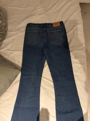 Levi's blå bootcut jeans - Ett par klassiska blå Levi's jeans med bootcut passform. Jeansen har mid waist och tillverkade i slitstark denim. Snygga kontrastsömmar och den ikoniska läderlappen bak i midjan. Perfekta för en avslappnad och trendig look.