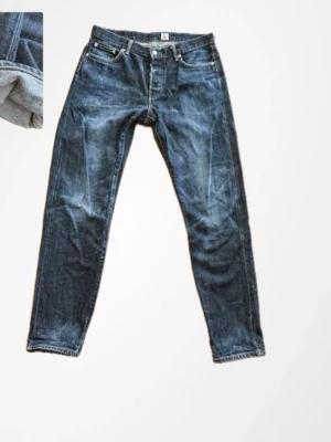 Edwin japanska Selvedge Jeans - Snygga japanska Edwin jeans i mörkblå denim med klassisk femficksdesign och orange kontrastsömmar. Jeansen har rak passform och selvedge-detalj vid benslutet. Tillverkade i Japan av robust bomullsjeans, perfekta för dig som gillar stilrena och tidlösa jeans.W31 L32