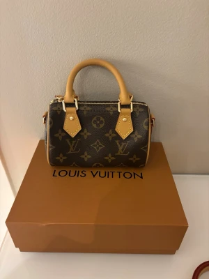 Louis Vuitton Monogram handväska - Säljer en snygg handväska från Louis Vuitton i klassiskt monogrammönster. Väskan är brun med ljusbruna handtag och detaljer i läder samt guldfärgade metalldetaljer. Perfekt accessoar för dig som gillar lyxiga märken och tidlös design.
