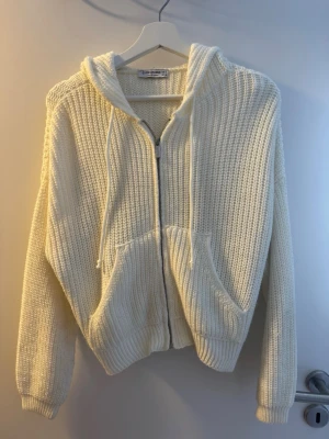 Vit stickad hoodie från Stradivarius - Mysig vit stickad hoodie från Stradivarius med dragkedja framtill och två stora fickor. Tröjan har huva med dragsko och ribbade muddar vid ärmslut och nederkant. Perfekt för lager på lager och chill dagar.