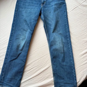 Blå raka jeans i klassisk modell H&M - Säljer ett par blå jeans med rak passform och klassisk femficksdesign. Jeansen har normal midja och är tillverkade i denim med lätt tvättad look. Perfekta för en avslappnad stil och passar till det mesta. Inget synligt märke på jeansen.
