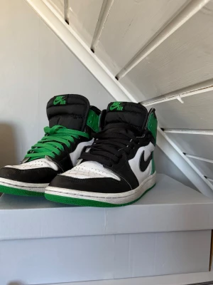 Nike Air Jordan 1 sneakers svart/vit/grön - Storleken är 41 på båda dessa Nike Air Jordan 1 sneakers i svart, vitt och grönt med klassisk Swoosh på sidan. Höga skaft och gröna samt svarta skosnören. Ikonisk Air Jordan-logga på plösen och gröna detaljer runt ankeln. Perfekta för dig som gillar streetwear och vill sticka ut. Men även ett par Nike air Jordan 1 sneakers i svart vit och blått.