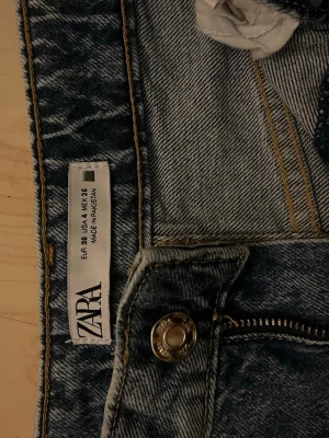 Blå raka jeans från ZARA - Snygga blå jeans från ZARA i klassisk tvätt med raka ben och femficksmodell. Jeansen har gylf med dragkedja och knapp, samt kontrastsömmar. Perfekta för en avslappnad och trendig look.