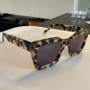 Leopardmönstrade solglasögon - Leopardmönstrad båge och breda skalmar. Modellen har en fyrkantig retroform och mörka glas🤎