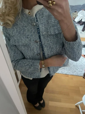 Blå tweed cardiganjacka med fickor - Snygg blåmelerad cardiganjacka i tweed med rund halsringning och dekorativa fickor framtill. Jackan har fransiga kanter och stängs med stora silvriga knappar. Perfekt att slänga över en tröja för en chic look. Storlek 40 men passar mer än xs-s.