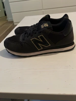 Svarta New Balance 500 sneakers - Säljer ett par svarta New Balance 500 sneakers med klassisk retrostil. Skorna har en stor vit N-logga på sidan, svart ovandel i mesh och syntet samt vit sula med svart yttersula. Perfekta för dig som gillar streetwear och sportig look.