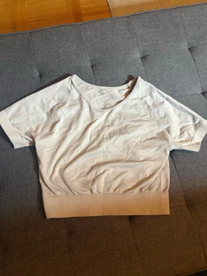 Vit croppad topp från ICIW - Säljer en vit croppad topp från ICIW med korta ärmar och bred ribbad kant nedtill. Toppen har en rund halsringning och är tillverkad i ett mjukt, stretchigt material som passar perfekt till träning eller en avslappnad look.