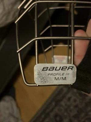 Bauer Profile III hockeygaller M - Säljer ett Bauer Profile III hockeygaller i storlek medium. Gallret är i metall med en klassisk silvrig färg och har svarta justerbara remmar på sidorna. Perfekt för dig som behöver extra skydd till hockeyhjälmen.