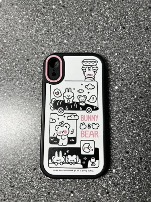 Sött mobilskal Bunny & Bear svart/vitt - Mobilskal med gulligt motiv av kanin och björn i seriestil, texten 'Bunny & Bear' i rosa. Skalet är svart med vit baksida och rosa detalj runt kamerahålet. Tillverkat i tålig plast, passar iPhone XR. Använd fast fortfarande på bra skick.