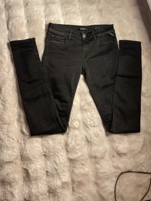 Svarta luz jeans från REPLAY - Snygga svarta skinny jeans från Replay, modell Luz. Jeansen har klassisk femficksdesign, normalhög midja och smala ben. Tillverkade i stretchigt material för skön passform. Perfekta till en trendig och avslappnad stil. W27 och L32 även om lappen är sönder så passar den till W27
