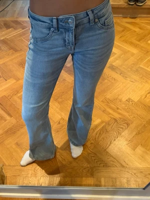 Ljusblå bootcut jeans - Säljer ett par ljusblå bootcut jeans med klassisk femficksdesign och normalhög midja. Jeansen har en snygg tvätt och är tillverkade i mjukt denimtyg med lite stretch för extra komfort. Perfekta för en avslappnad och trendig look.