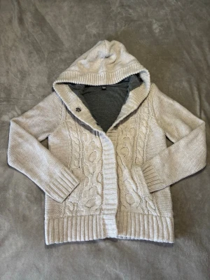 Beige stickad cardigan - Mysig beige stickad hoodie med kabelstickat mönster framtill. Tröjan har ribbade muddar, två fickor och knappar framtill. Perfekt för lager-på-lager och chill dagar. Materialet är mjukt och värmande, och luvan ger extra komfort. Skriv vid funderingar och mått!!