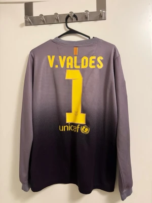 Barcelona målvaktströja V. Valdes - Snygg långärmad målvaktströja från FC Barcelona med V. Valdes och nummer 1 på ryggen. Tröjan är grå och svart med gula detaljer, klubbmärke och sponsorer på bröstet. Tillverkad i funktionsmaterial som andas, perfekt för fotbollsträning eller match. Size XL boys eller S men 