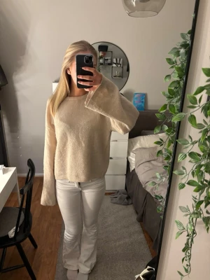 Beige stickad tröja med vida ärmar - Mysig beige stickad tröja med rund halsringning och extra vida ärmar. Tröjan har en rak passform och är tillverkad i ett mjukt, fluffigt material som känns skönt mot huden. Perfekt för lager-på-lager och en avslappnad stil.