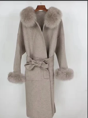 Helt ny äkta pälskappa  - Stilren beige kappa med stora pälsdetaljer vid krage och ärmslut. Kappan har knytband i midjan för en snygg siluett och är tillverkad i ett mjukt tyg som ger en lyxig känsla. Perfekt för dig som vill ha en trendig och elegant look. Storleken är mer onesize. 